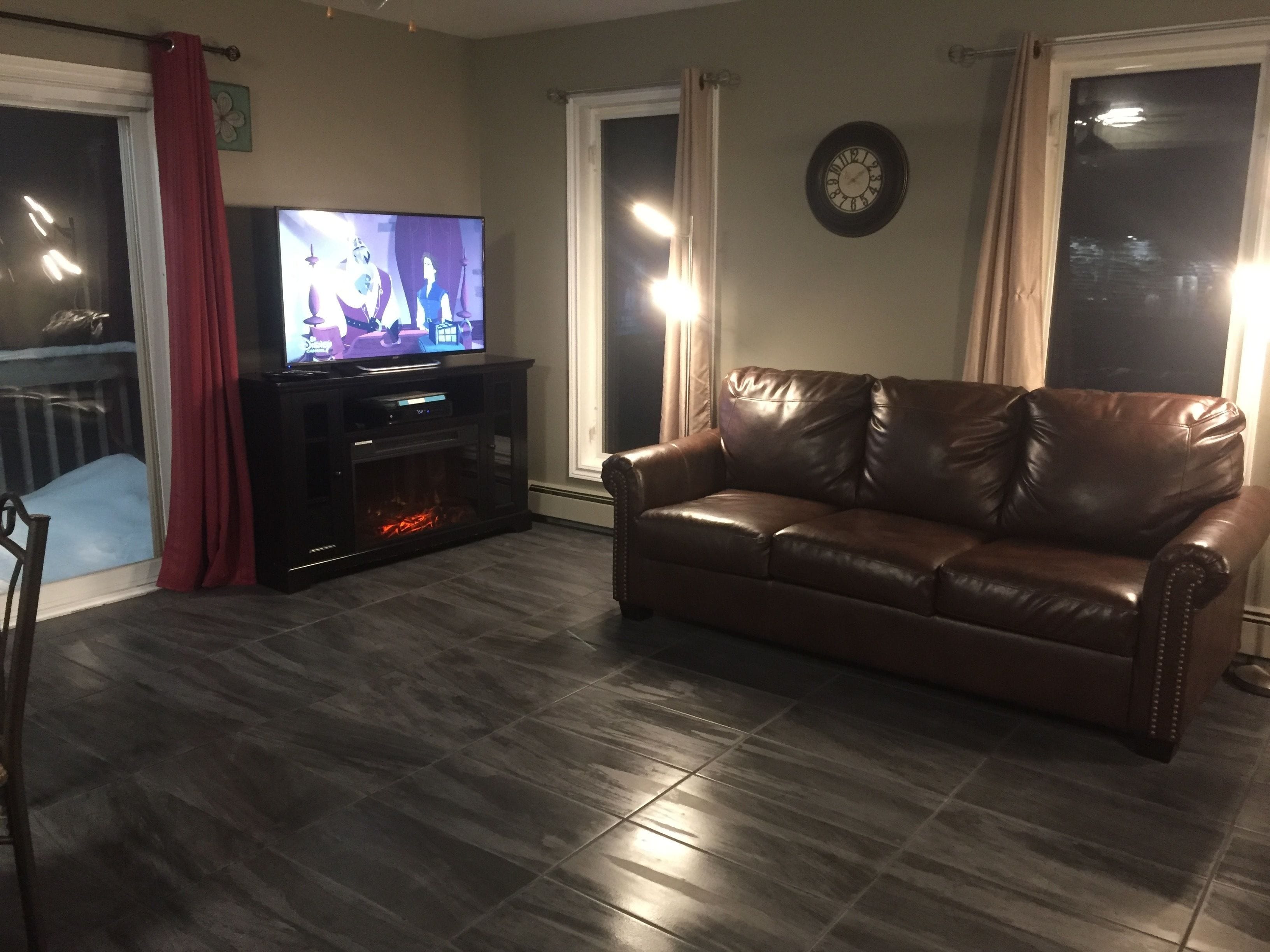 Een woonkamer met een leren bank, een flatscreen televisie, een open haard en een klok aan de muur.