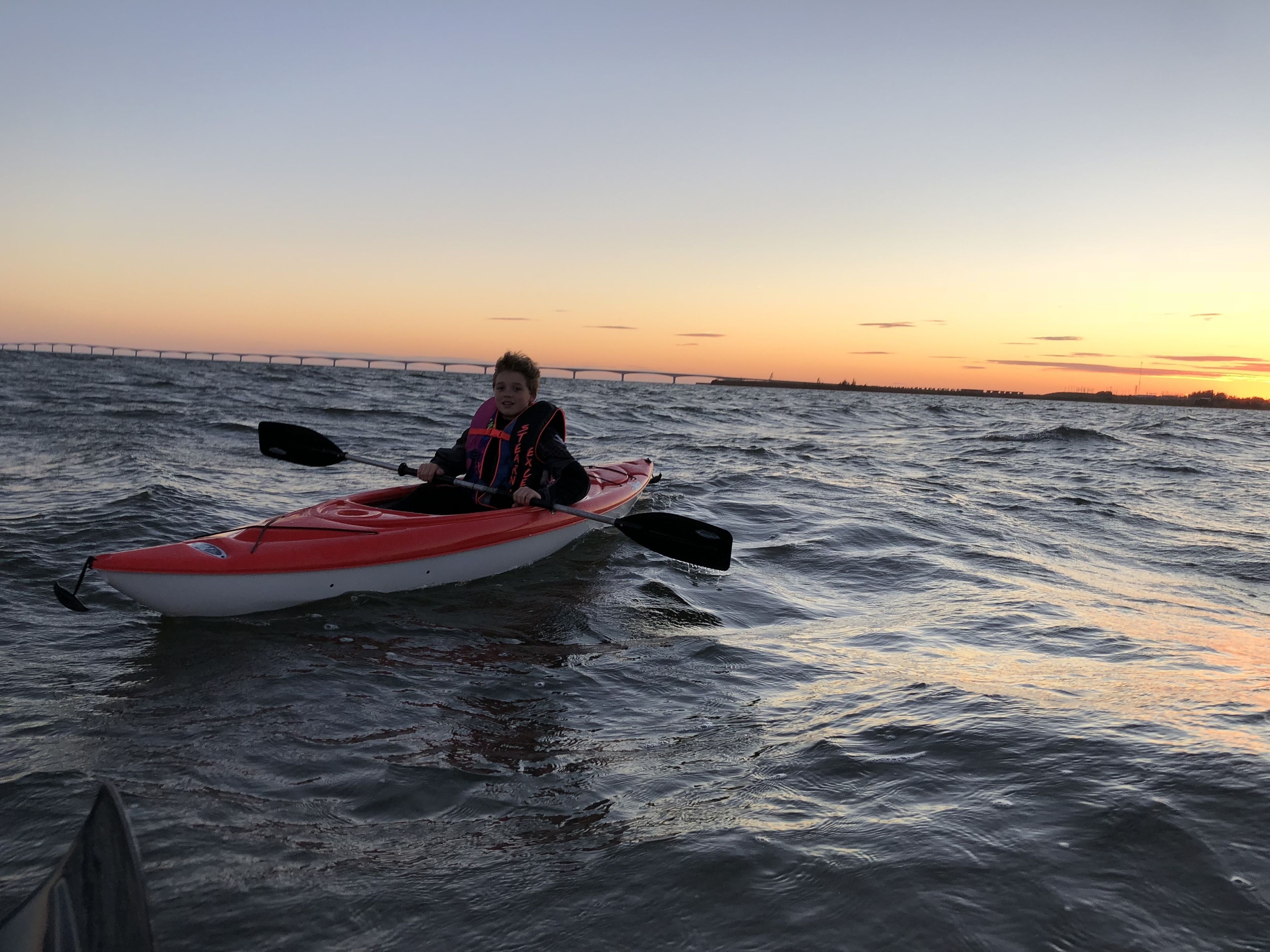 A person in a red kayak on a body of water with a sunset in the background.