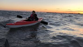 A person in a red kayak on a body of water with a sunset in the background.