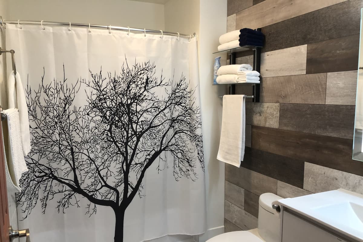 Un baño con un adhesivo de árbol en la cortina de la ducha, un inodoro y un perchero con toallas.