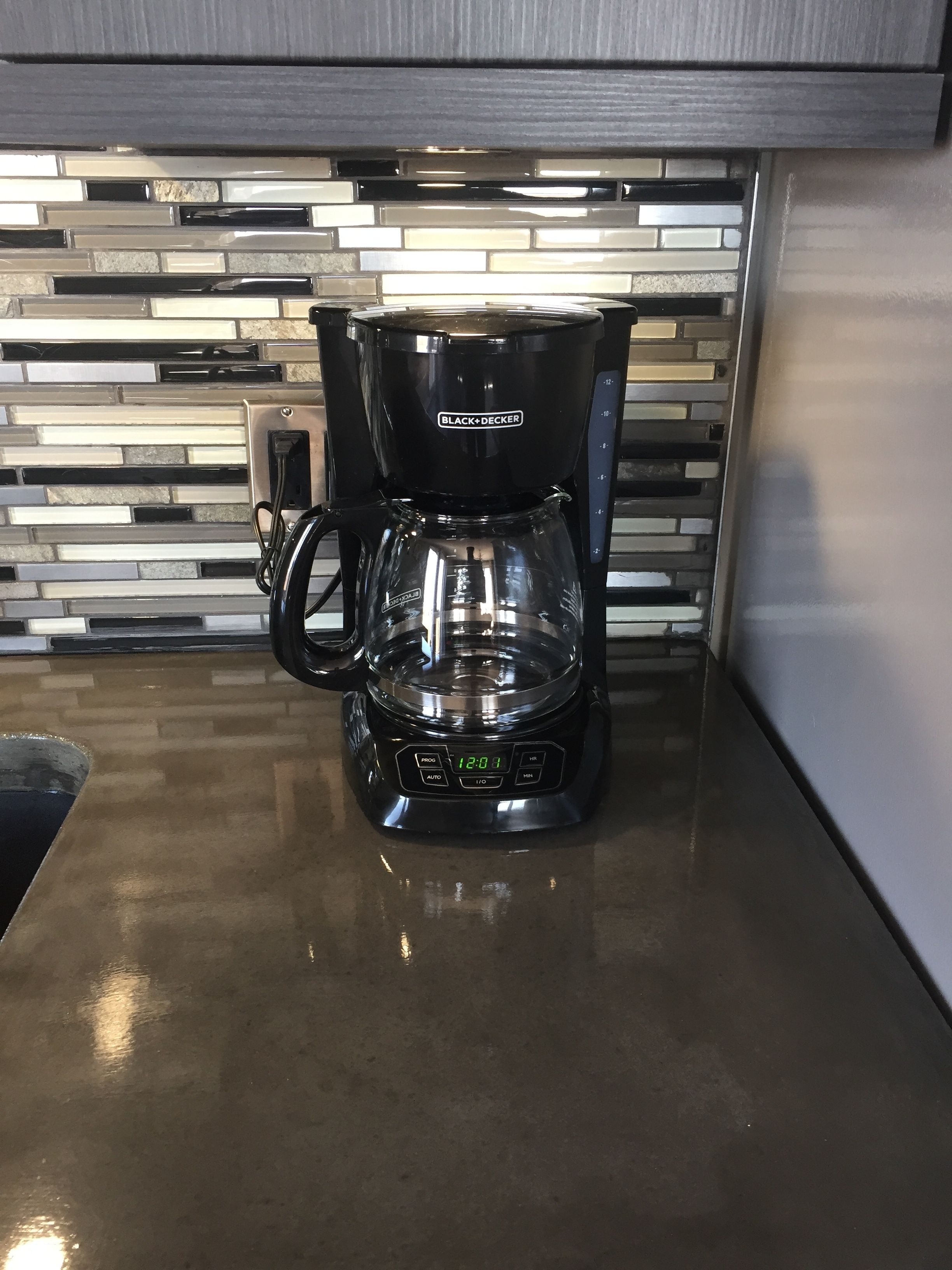 A black Black+Decker coffee maker on a kitchen counter with a modern tiled backsplash.