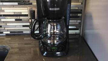 A black Black+Decker coffee maker on a kitchen counter with a modern tiled backsplash.