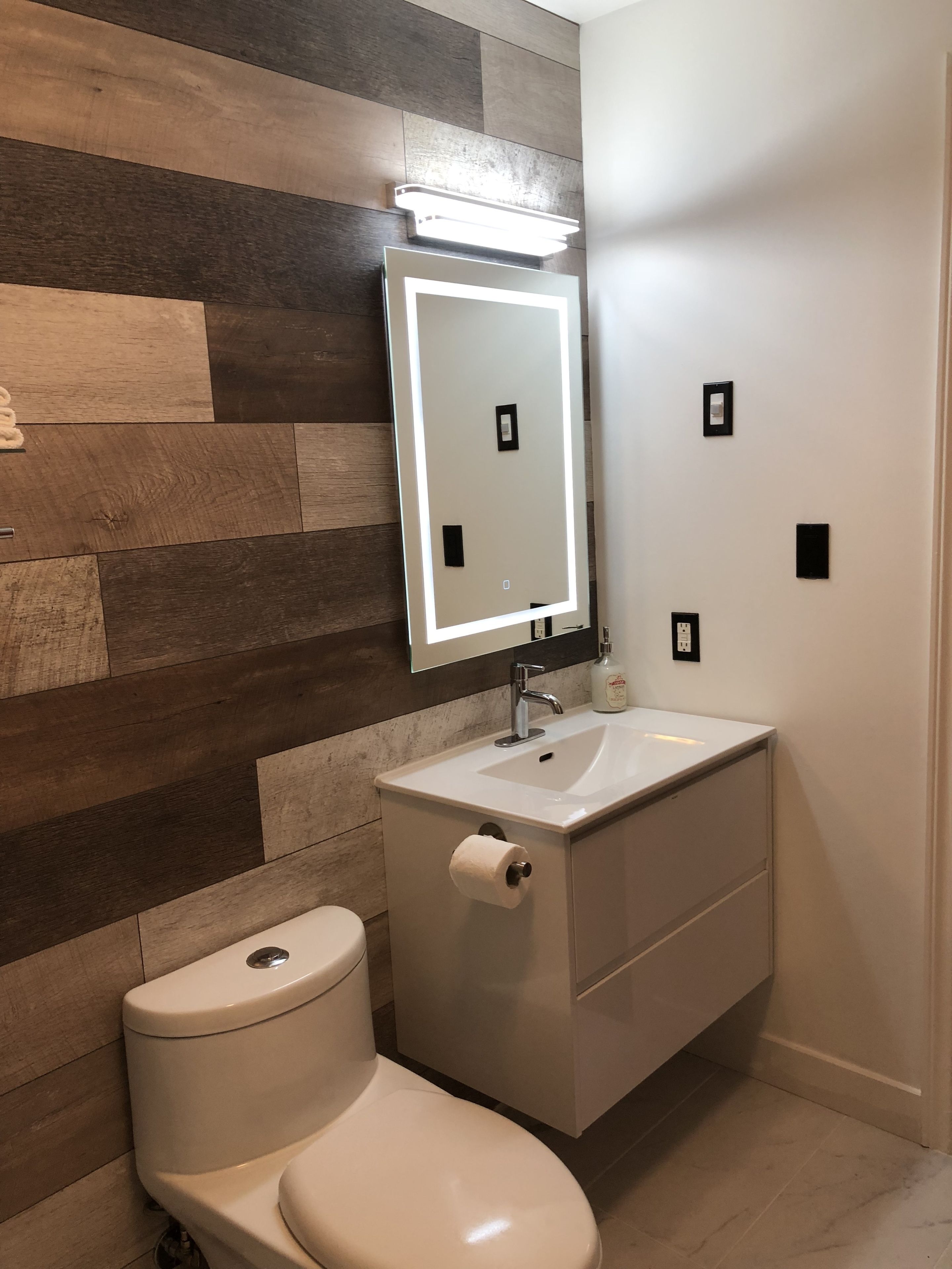 Ein Badezimmer mit Holzpaneele, einem weißen Waschbecken mit Spiegel und einer Toilette.