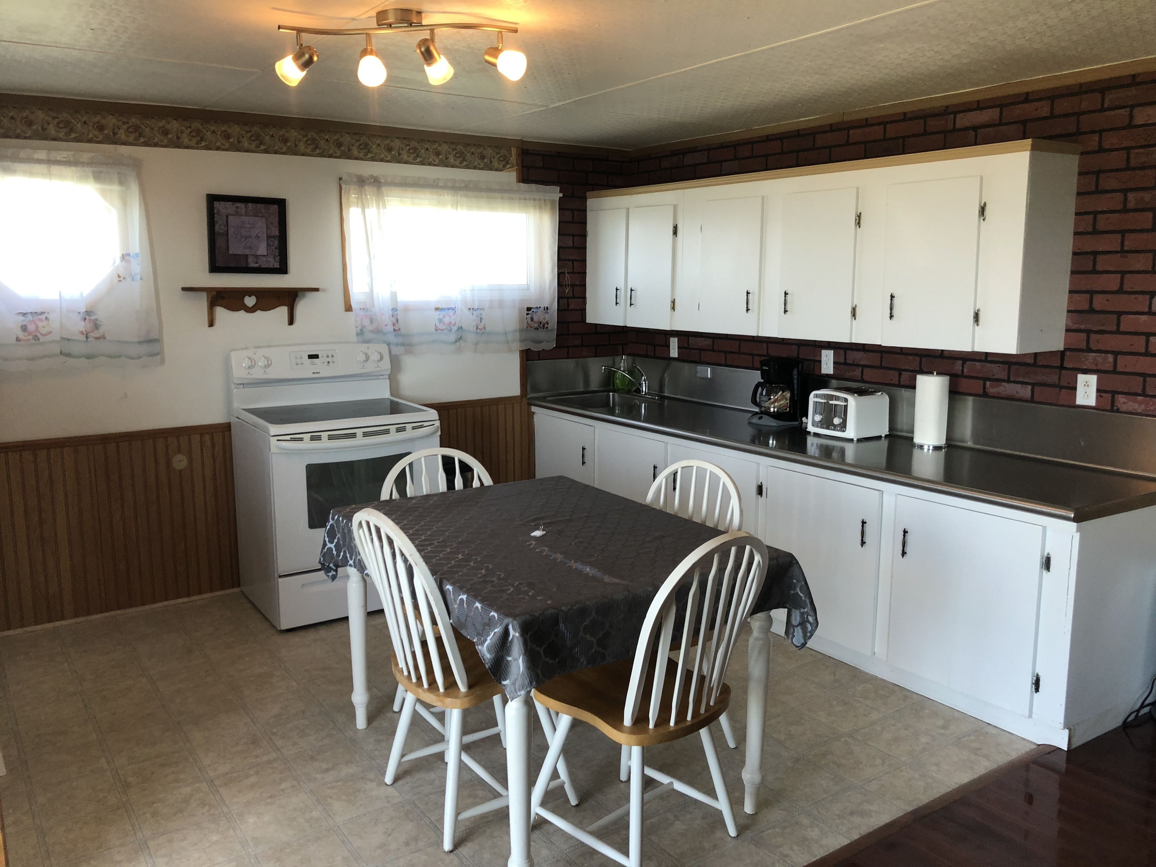 Una cocina compacta con armarios blancos, estufa, fregadero y una mesa de comedor con sillas.