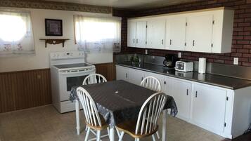 Una cocina compacta con armarios blancos, estufa, fregadero y una mesa de comedor con sillas.