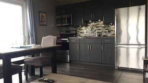 A modern kitchen with dark cabinets, stainless steel appliances, and a wooden dining table.