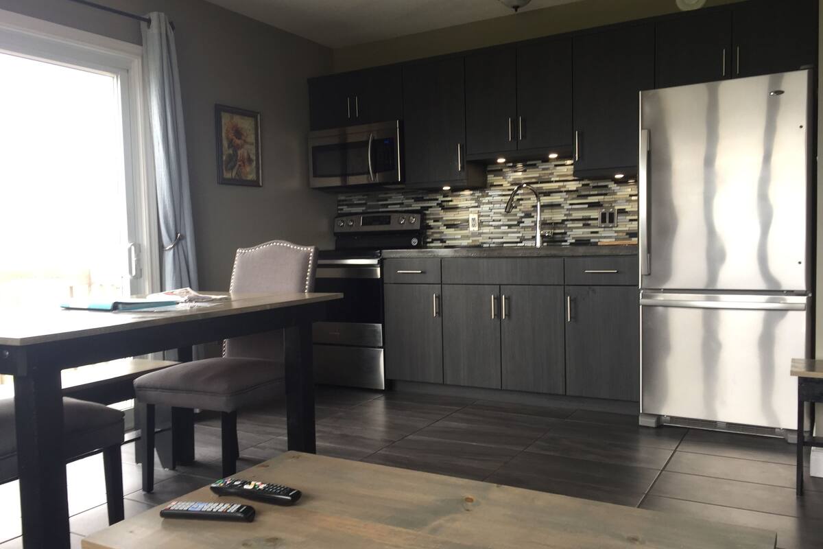 Una cocina moderna con armarios oscuros, electrodomésticos de acero inoxidable y una mesa de comedor de madera.
