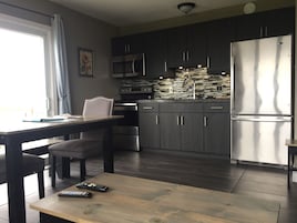 A modern kitchen with dark cabinets, stainless steel appliances, and a wooden dining table.