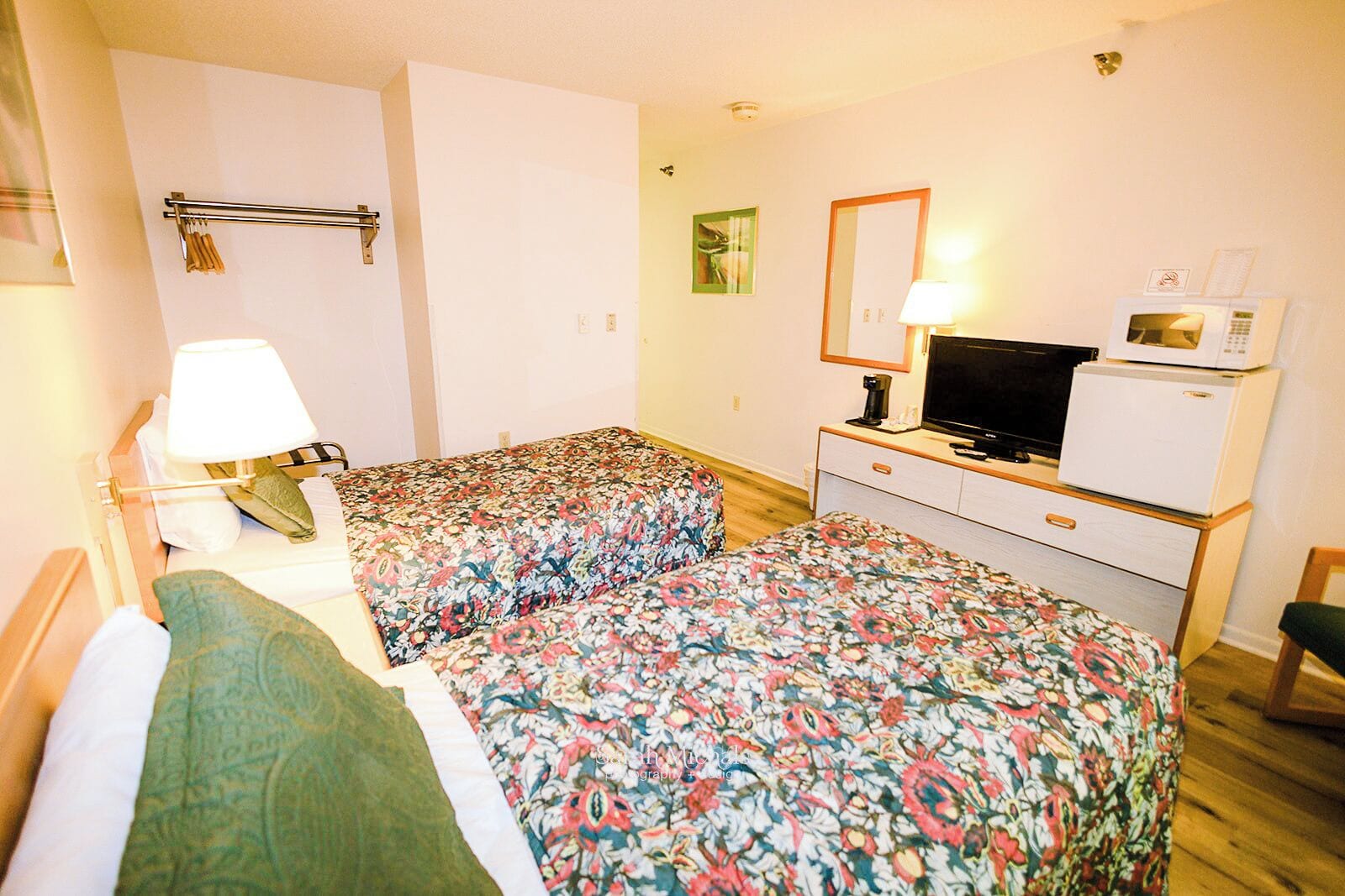 Une chambre d’hôtel avec deux lits, un bureau équipé d’une télévision et d’un micro-ondes, et une lampe.