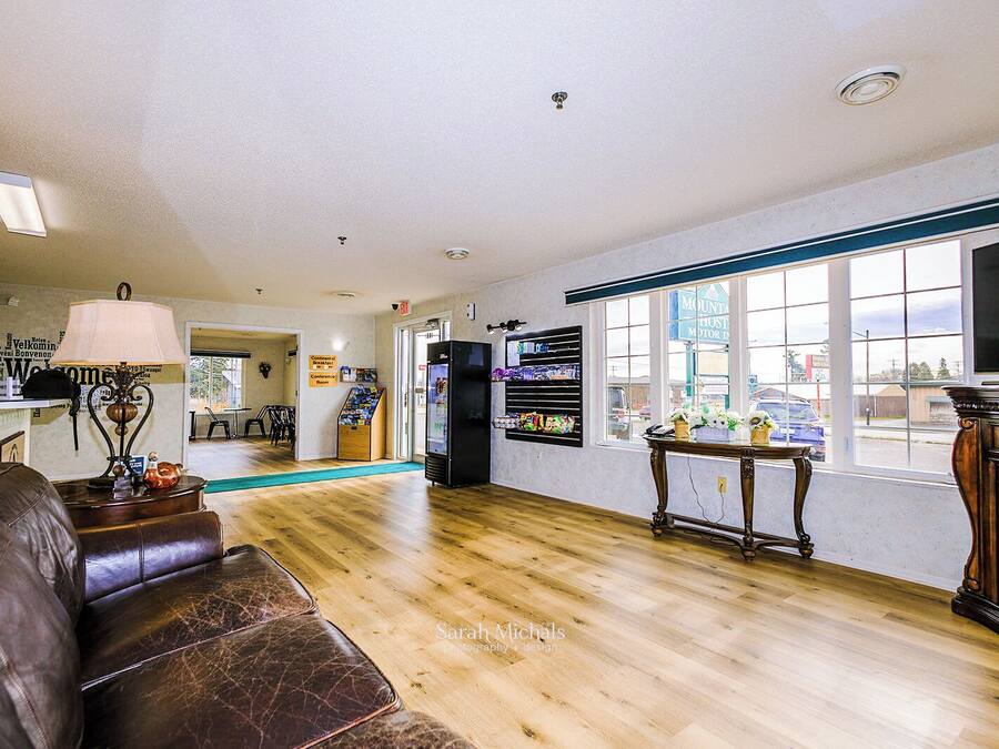 A spacious living area with a wooden floor, a leather couch, a television, and a refrigerator.