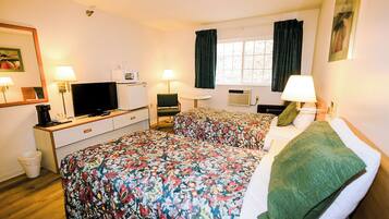 Een hotelkamer met twee bedden, een bureau met een televisie, een kleine koelkast en een raam met gordijnen.