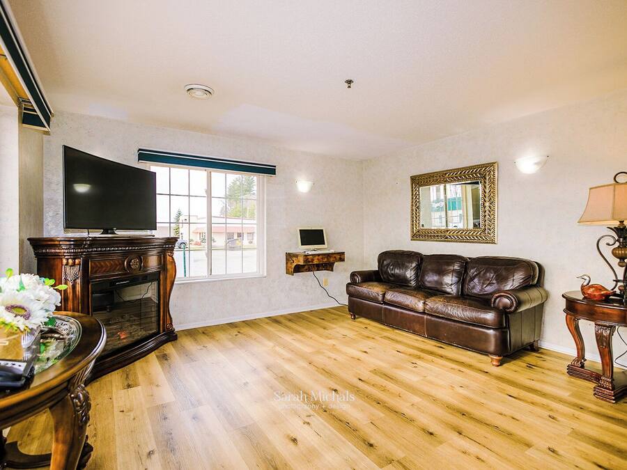 A living room with a wooden floor, a leather sofa, a television, a fireplace, and a window with a view of the outside.