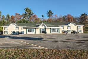 A two-story building with a green roof and beige walls, a parking lot in front, and trees in the background. - Mountain Host Motor Inn (Iron Mountain)