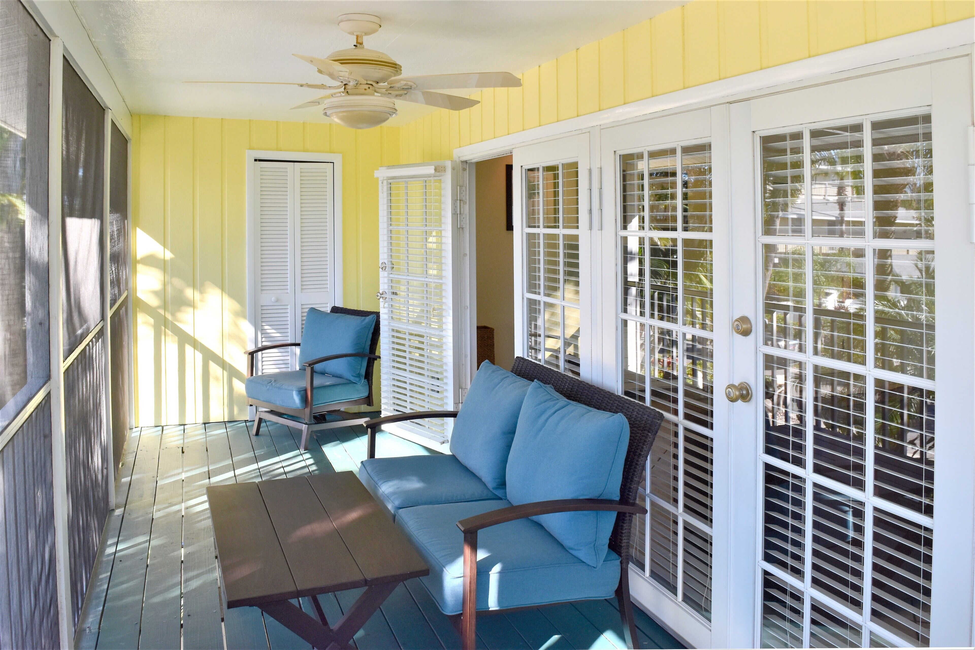 A covered porch with a blue sofa, a table, and a ceiling fan.
