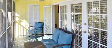 A covered porch with a blue sofa, a table, and a ceiling fan.