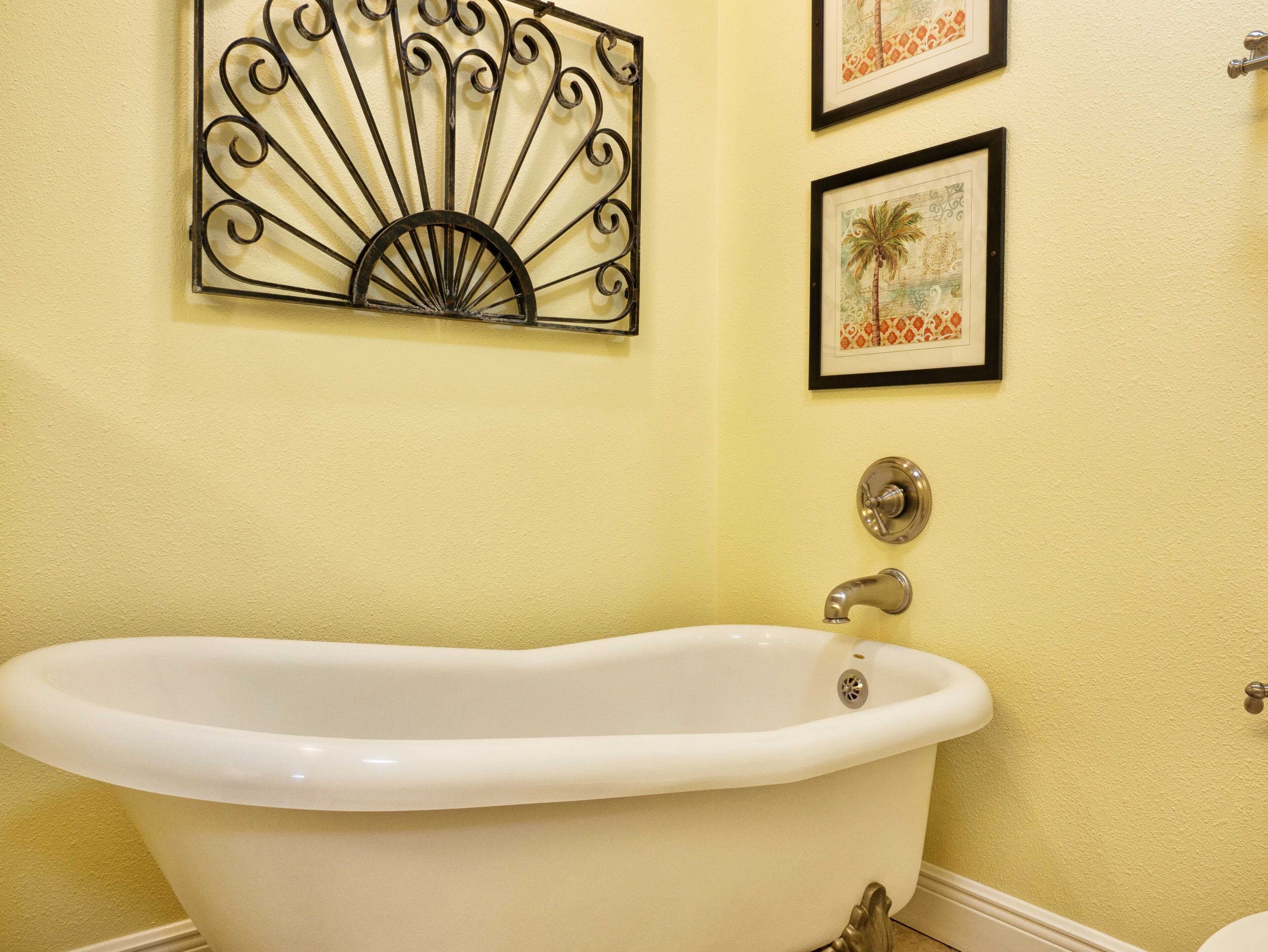 A bathroom with a freestanding bathtub, a wall-mounted fan, and two framed pictures.