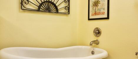 A bathroom with a freestanding bathtub, a wall-mounted fan, and two framed pictures.