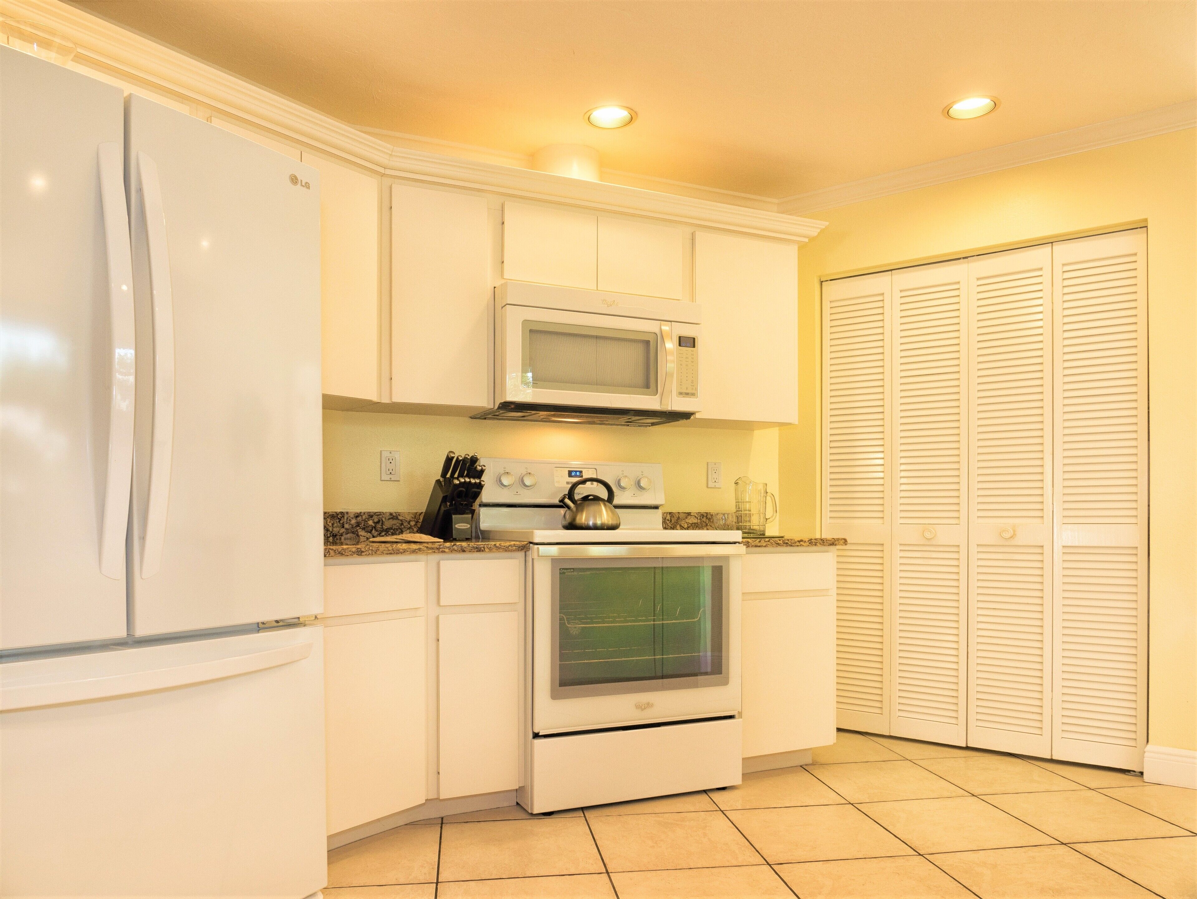 A compact kitchen with white cabinets, a built-in microwave, a kettle, and a refrigerator.