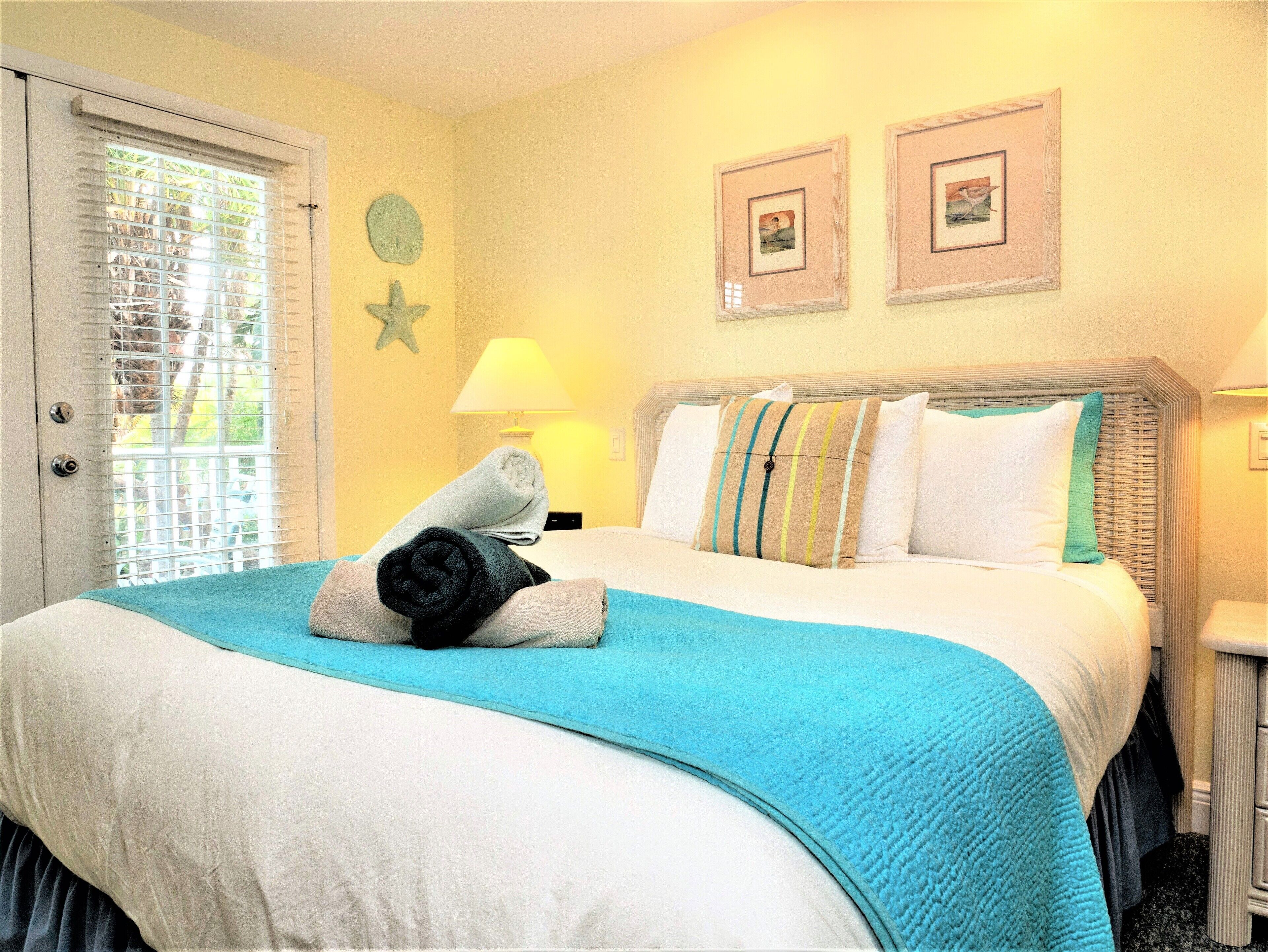 A hotel room with a bed, a nightstand, a lamp, and two framed pictures on the wall.