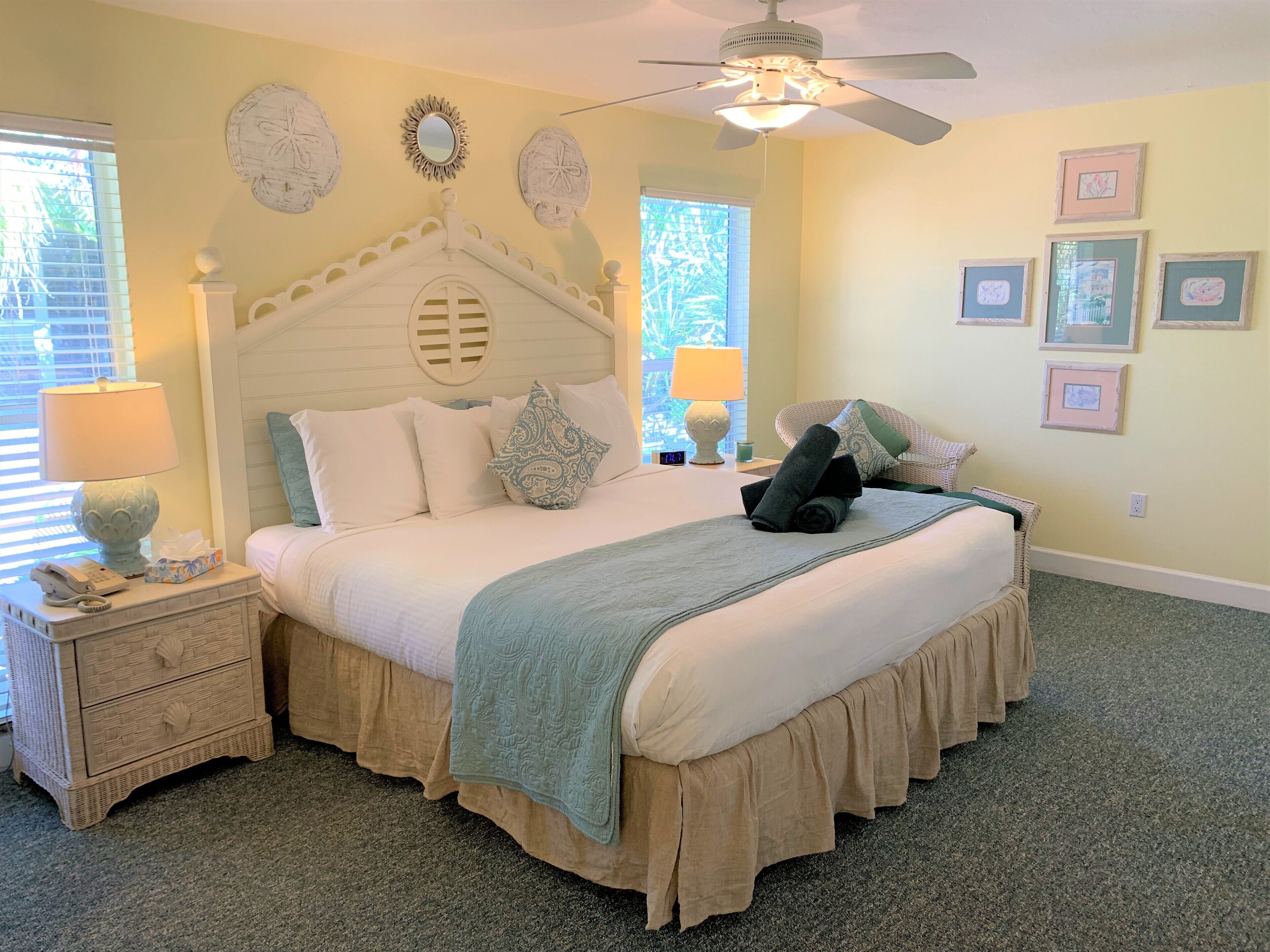 Une chambre bien rangée, avec un lit, des tables de chevet, un ventilateur de plafond et des décorations murales.