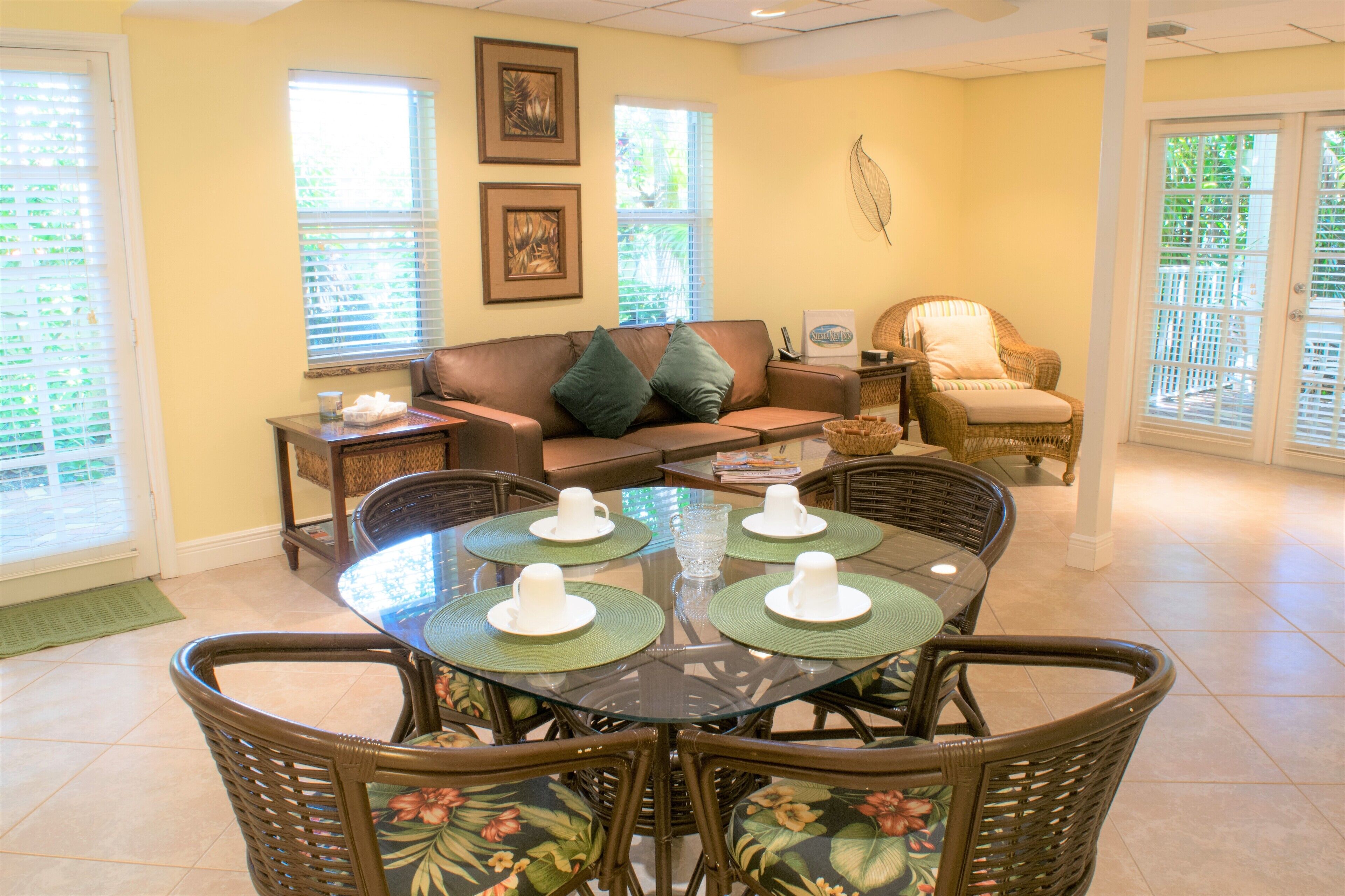 A dining area with a glass-top table, wicker chairs, and a brown leather sofa.
