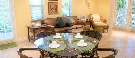 A dining area with a glass-top table, wicker chairs, and a brown leather sofa.
