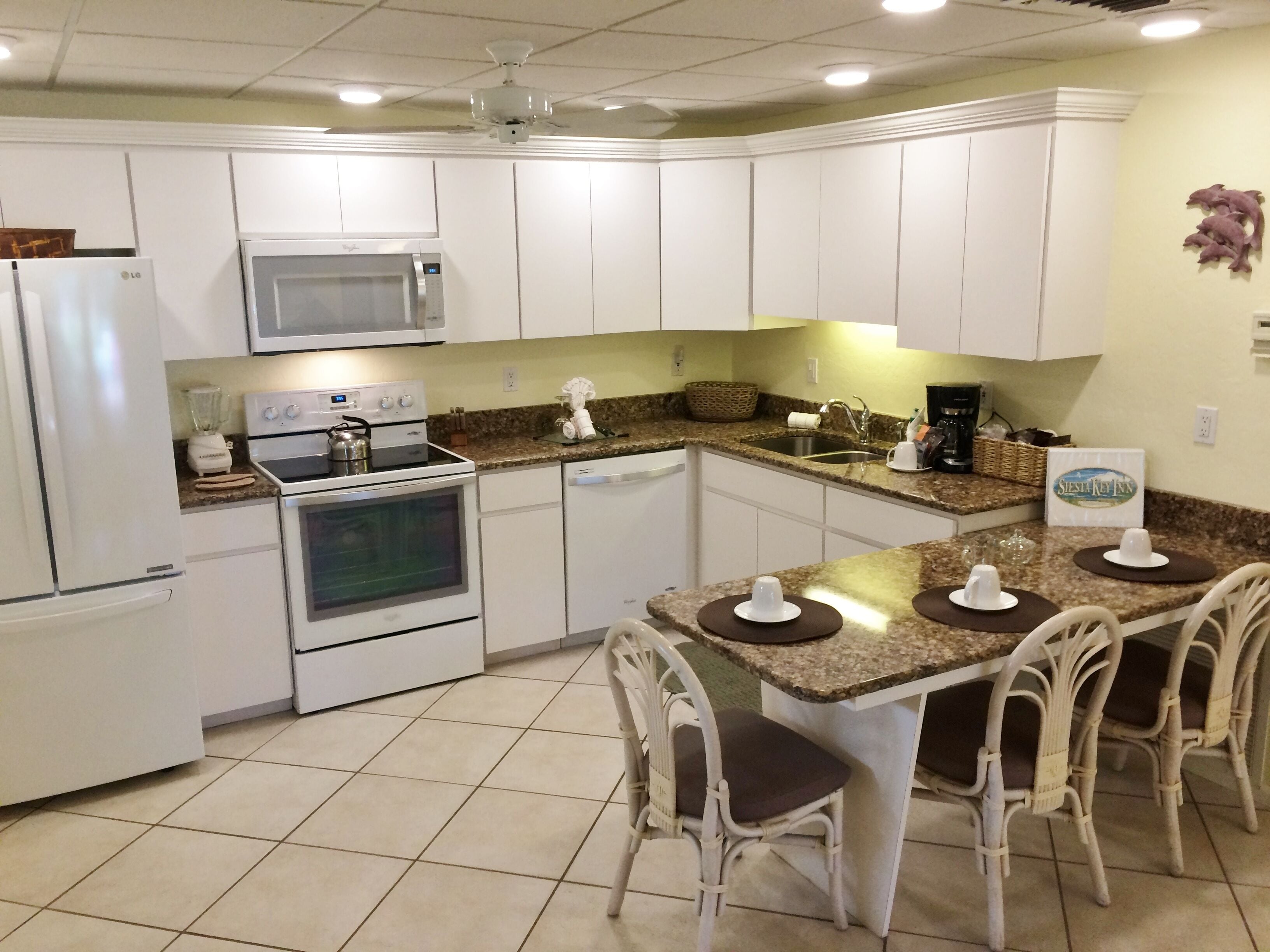A kitchen with white cabinets, a microwave, an oven, a dishwasher, a granite countertop, and a dining area with four chairs.