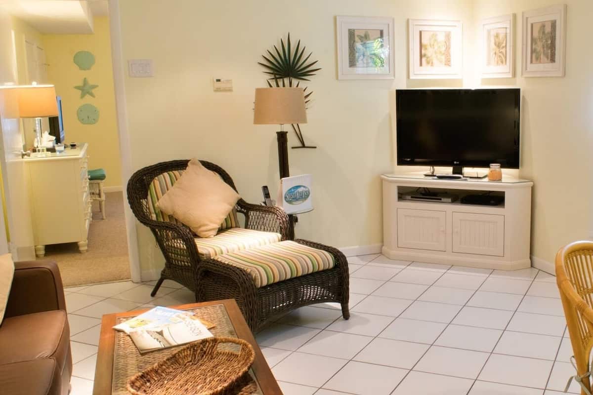A living room with a wicker chair, a television on a cabinet, and a small table with a basket.
