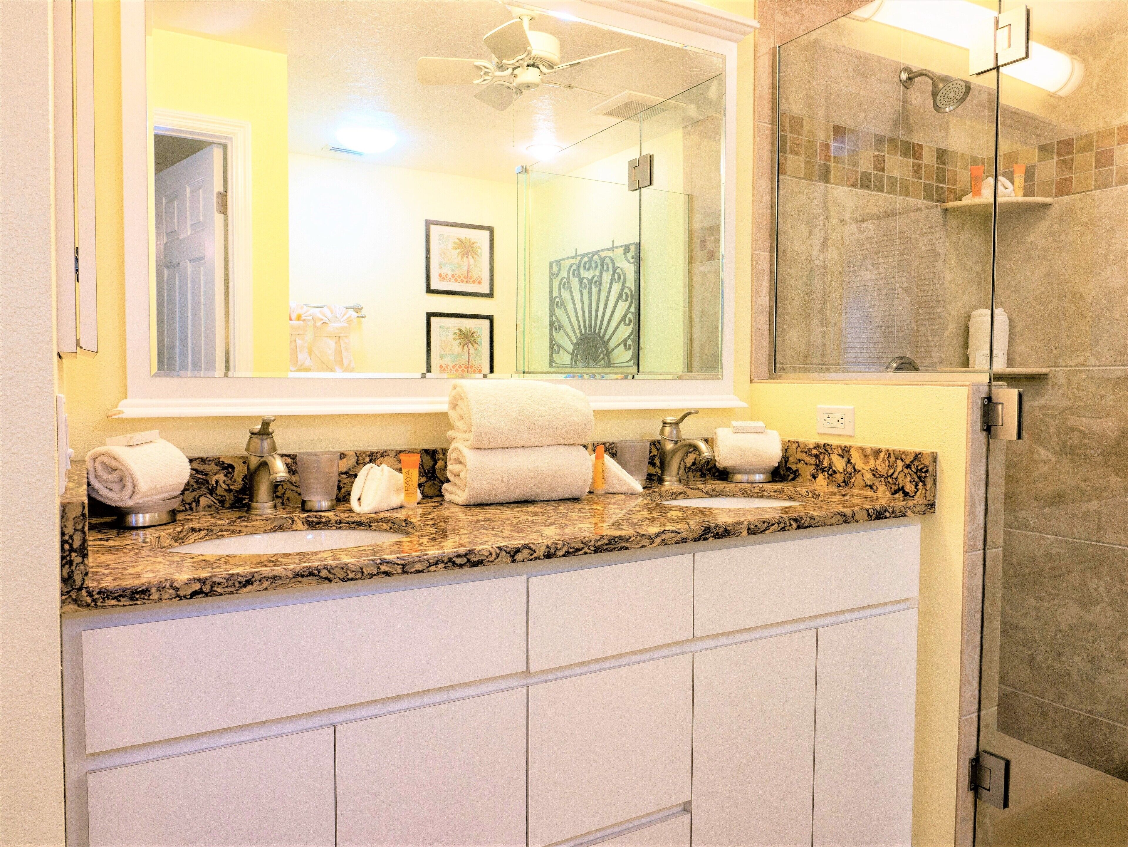 A bathroom with a granite countertop, a large mirror, a shower with a glass door, and a towel rack.
