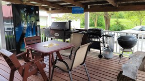 A covered outdoor patio with a grill, seating, and a view of the surrounding greenery. - Little River Inn Motel & Guest House (Leon)