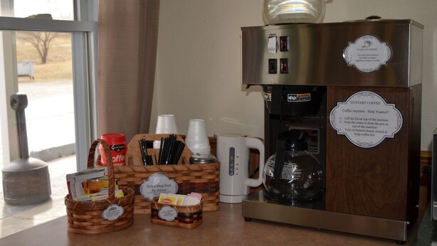 A coffee station with a coffee maker, cups, and a mug. There are baskets with coffee packets and a coffee pot on the counter. - Little River Inn Motel & Guest House (Leon)