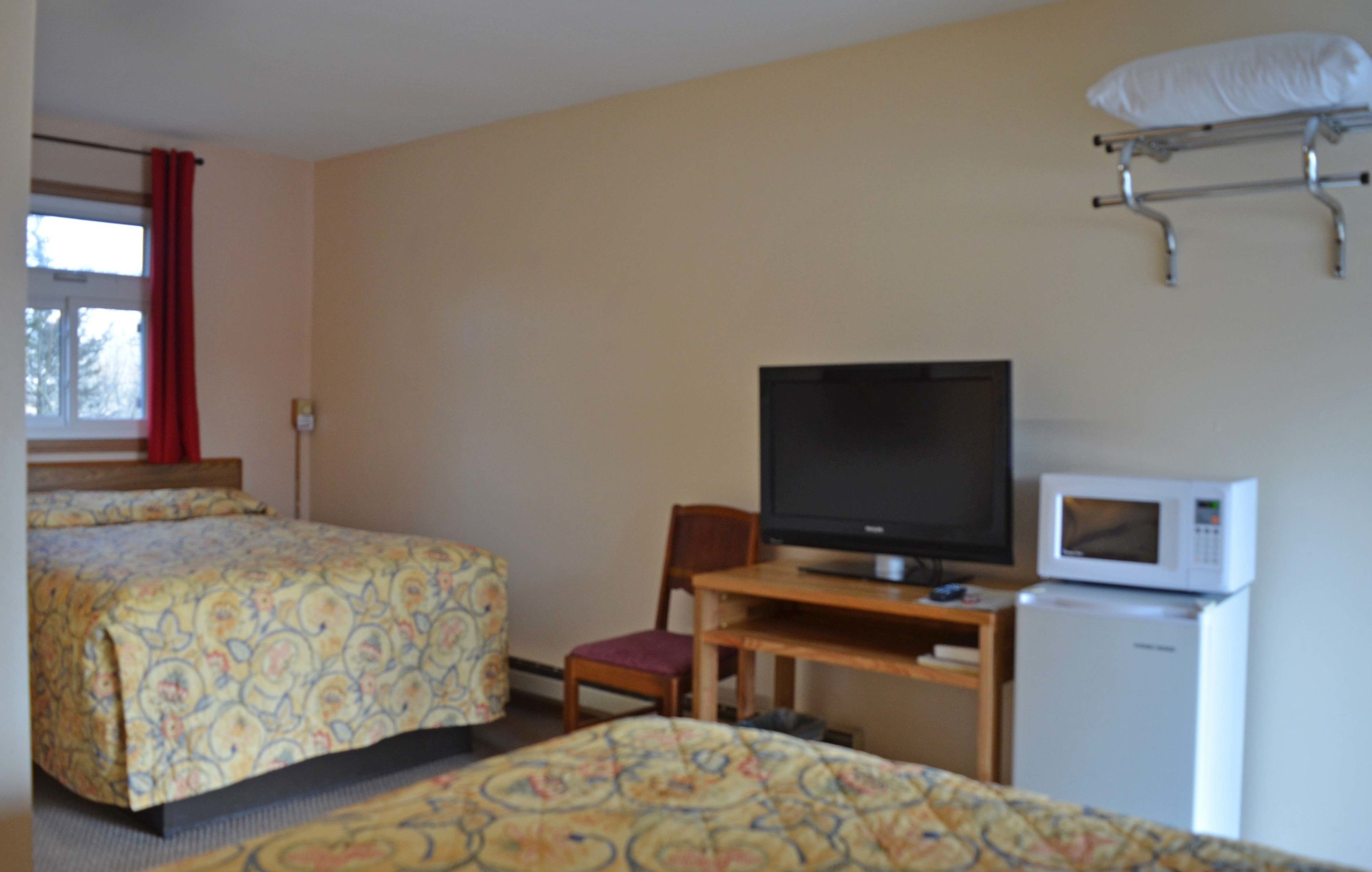 A hotel room with two beds, a television, a microwave, and a desk.