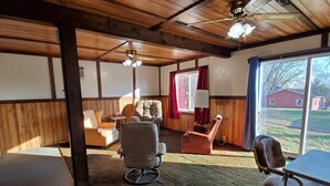A room with wooden walls and ceiling, a large window with a view of a red building, and a ceiling fan. - Little River Inn Motel & Guest House (Leon)