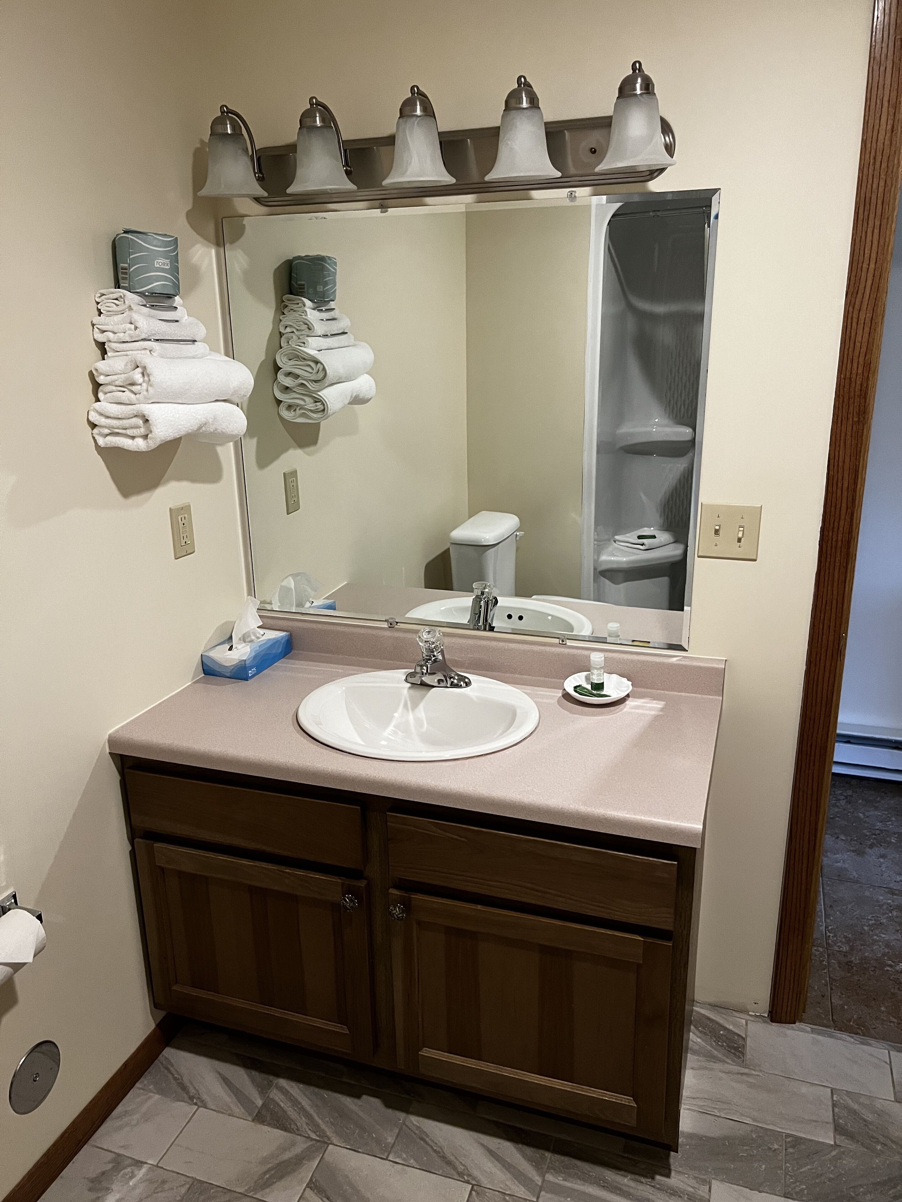 A bathroom with a sink, mirror, towel rack, and a toilet visible in the reflection.