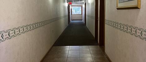 A long, narrow hallway with tiled floors and walls, leading to a door at the end.