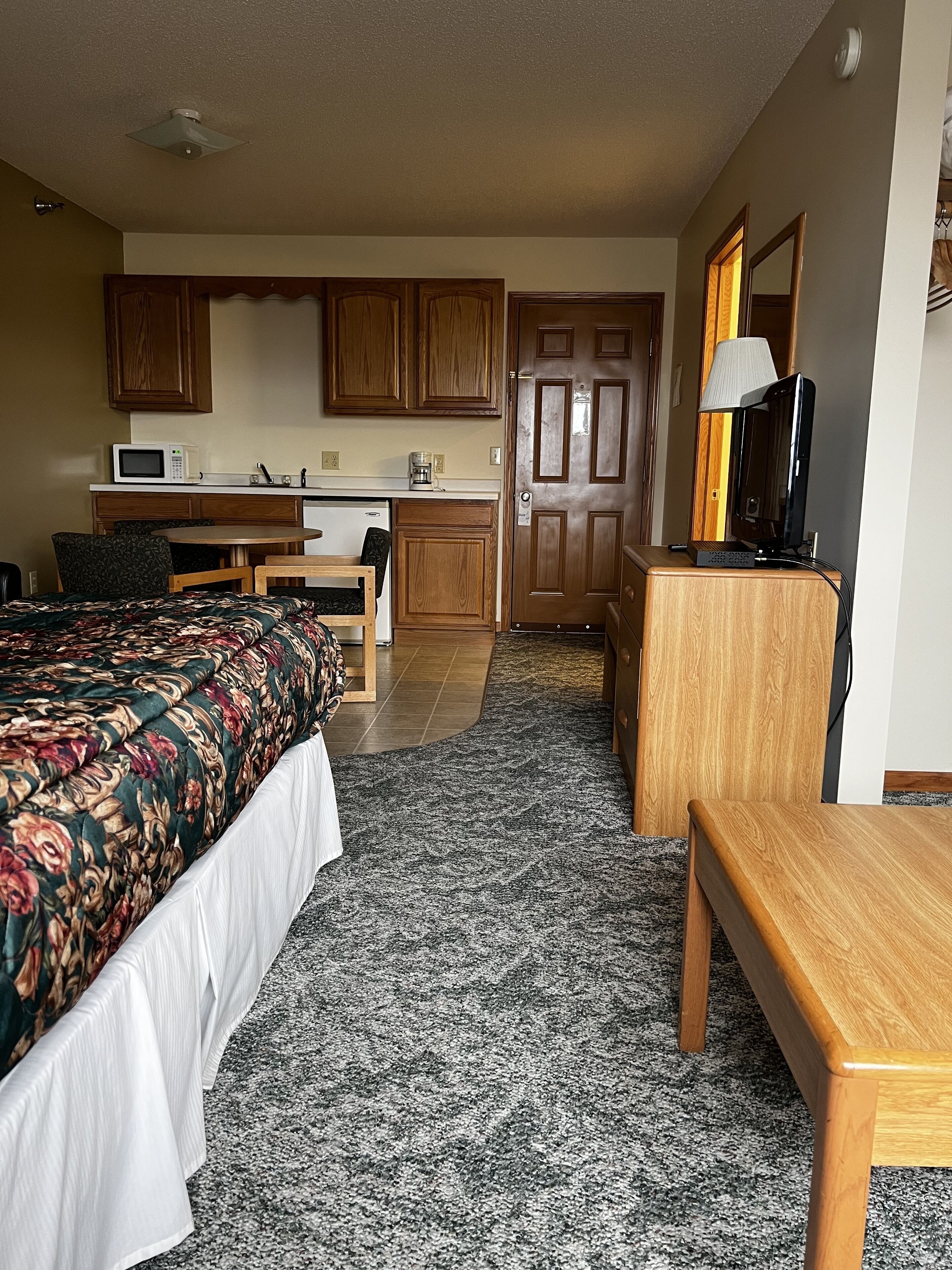 Una habitación de hotel compacta con cama, escritorio, kitchenette y televisor.
