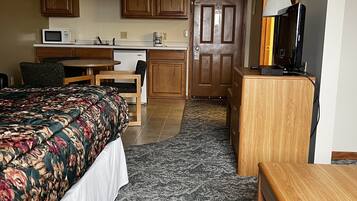 Una habitación de hotel compacta con cama, escritorio, kitchenette y televisor.