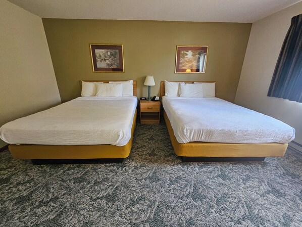 A hotel room with two beds, a nightstand, a lamp, and two framed pictures on the wall.