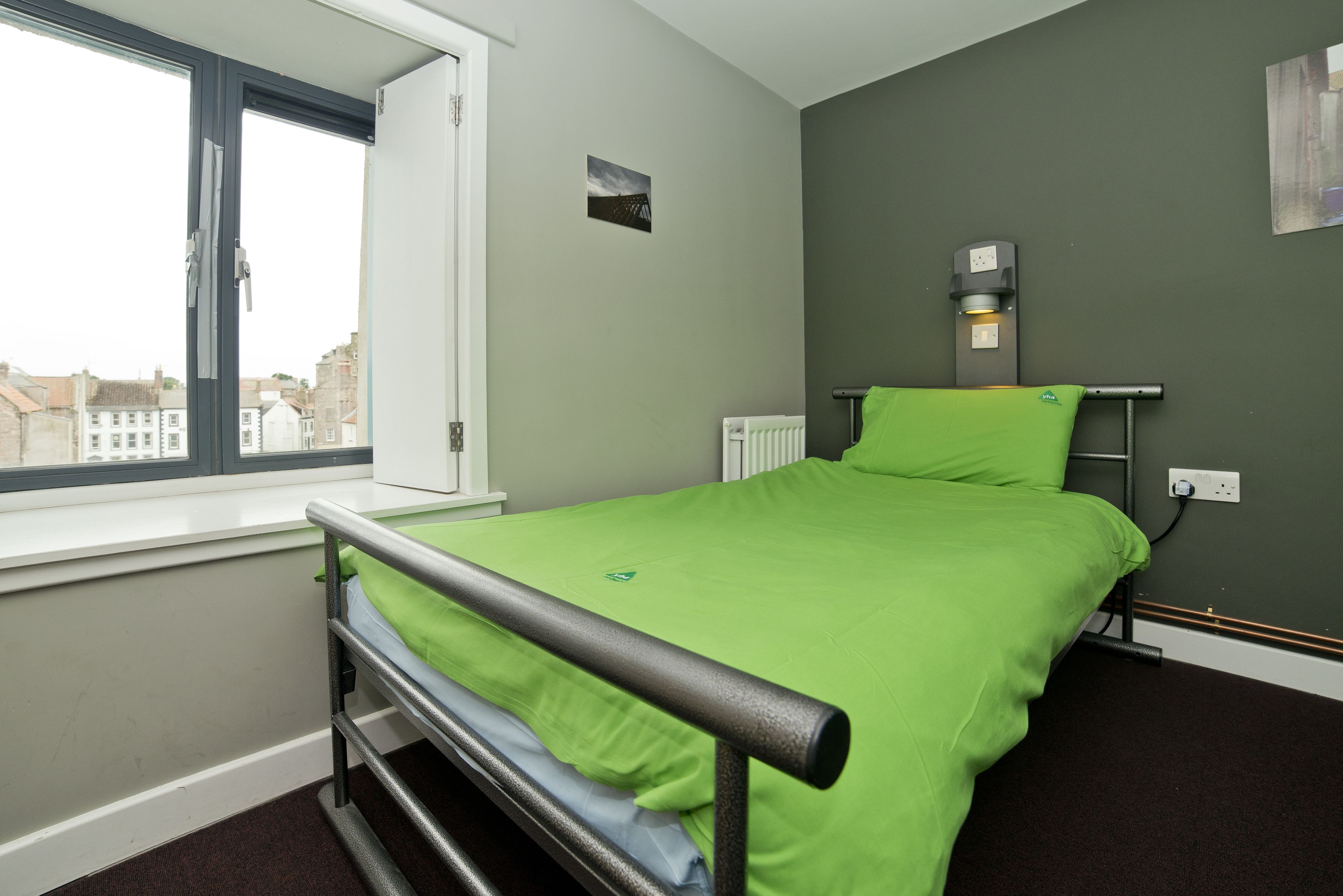 A room with a bed, a window, a radiator, and a wall-mounted light fixture.