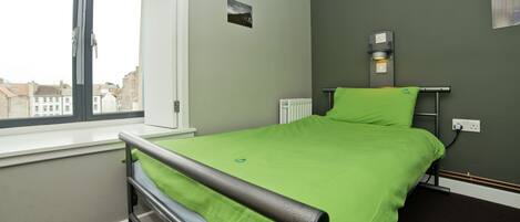 A room with a bed, a window, a radiator, and a wall-mounted light fixture.