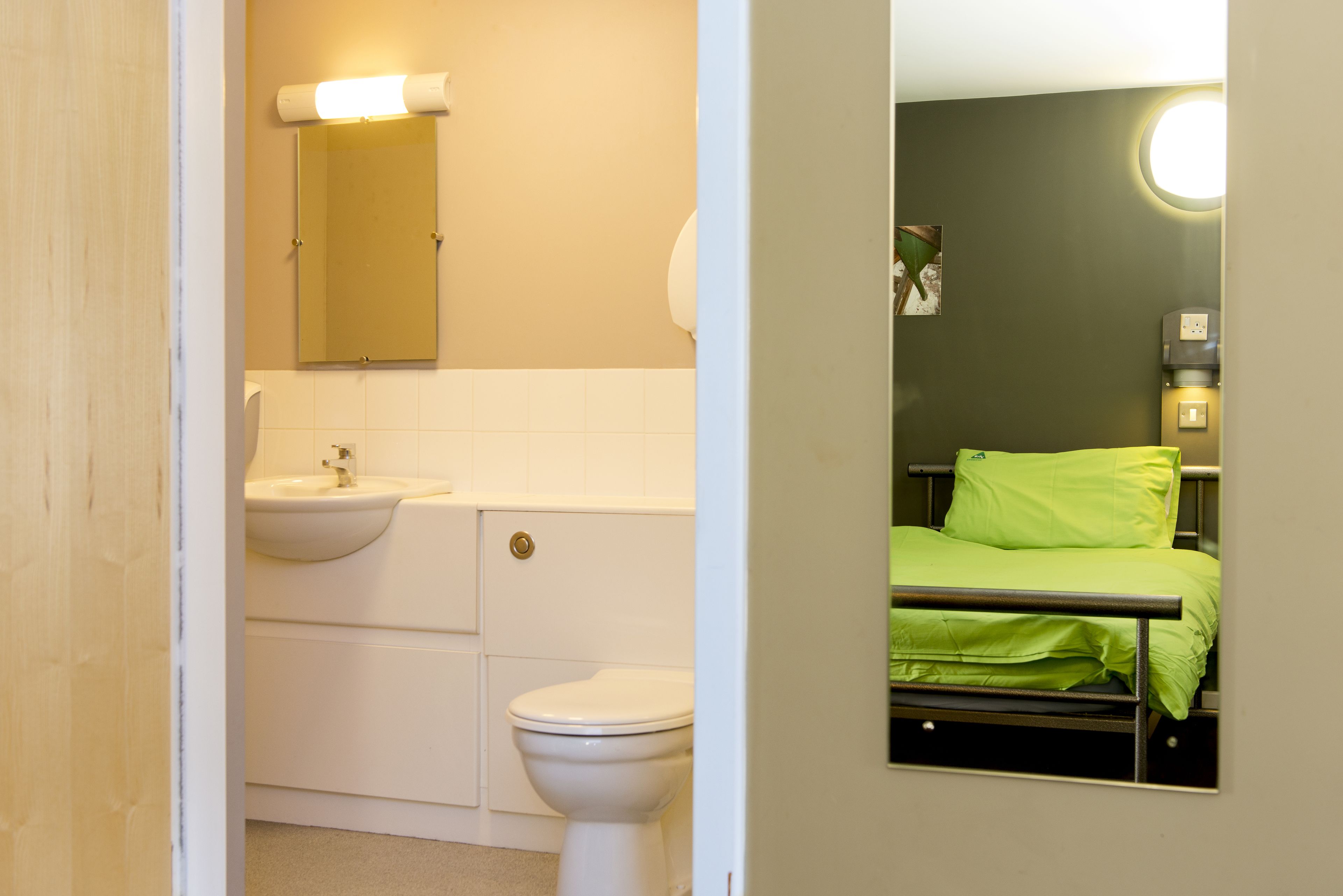 Un baño con lavamanos, inodoro y una cama con ropa de cama verde.