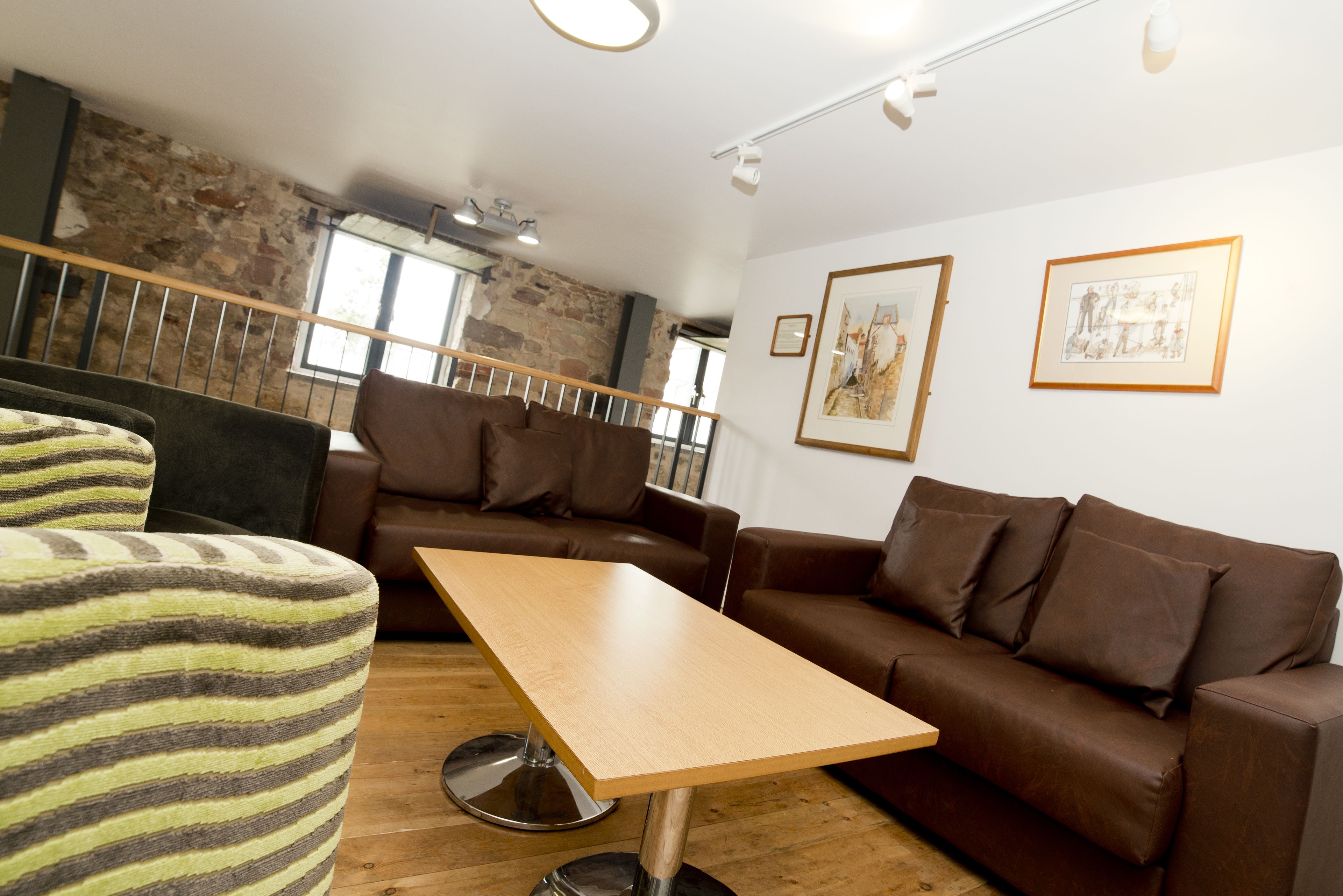 A modern living room with a wooden table, brown leather sofas, and a stone wall.