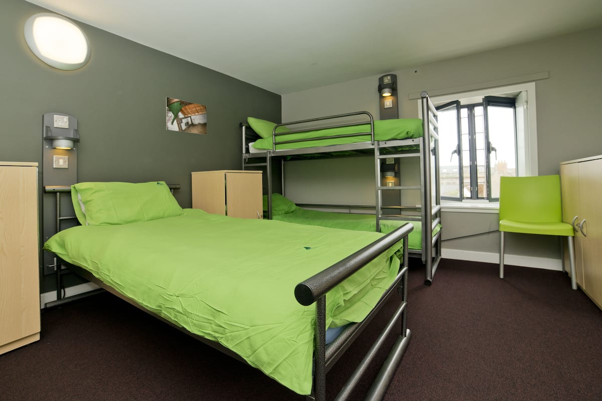 A bunk bed room with a desk and chair, a window, and a wall-mounted heater.