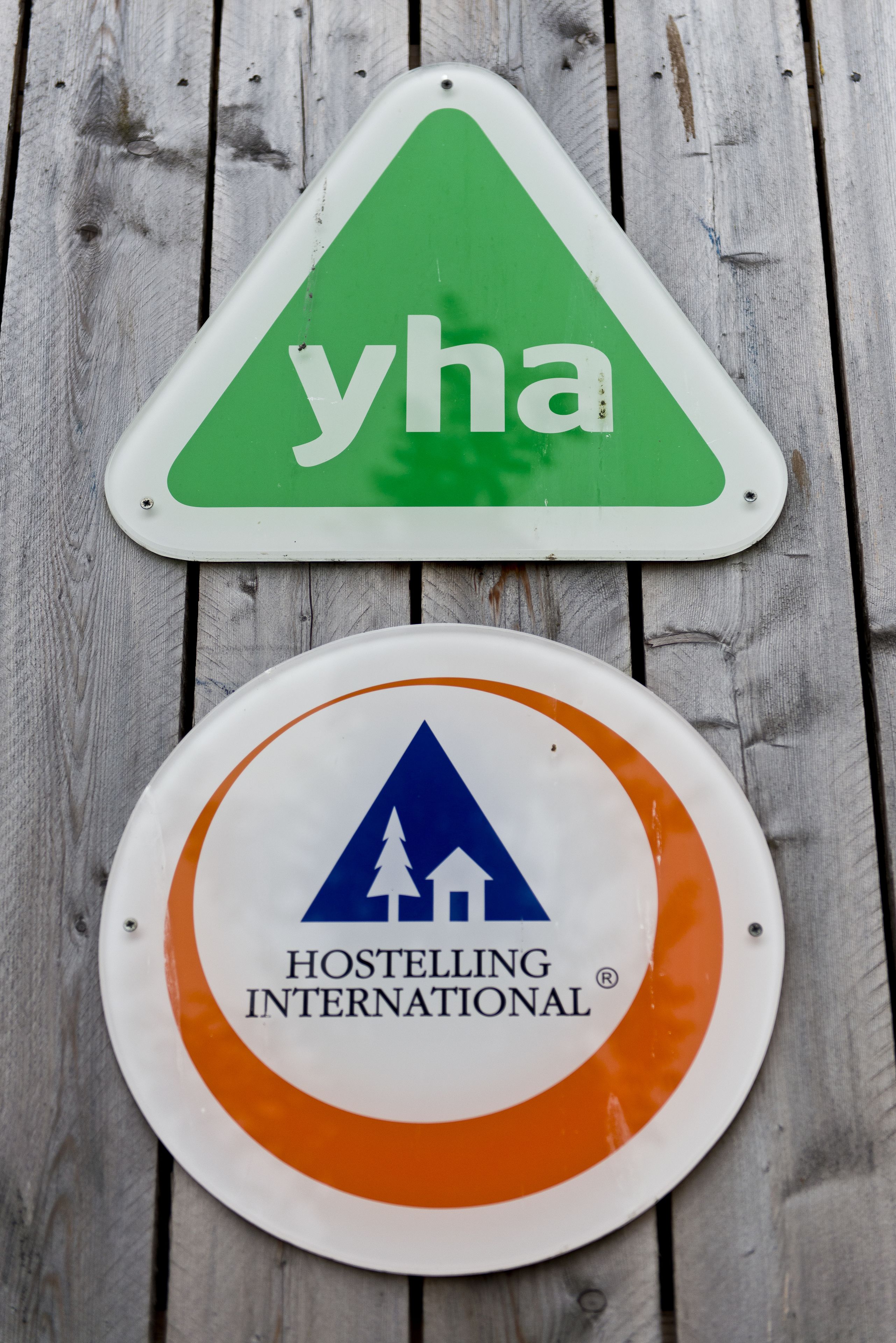 Dos carteles: uno verde con 'yha' y otro naranja con el logotipo de 'Hostelling International'.