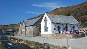 A stone building with a gabled roof by a water body, featuring a stone pathway and a small dock. - YHA Boscastle - Hostel (Boscastle)