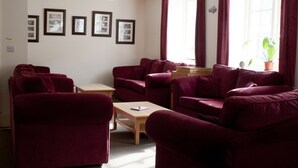 A living room with red sofas, a wooden coffee table, and framed pictures on the wall. - YHA Boscastle - Hostel (Boscastle)