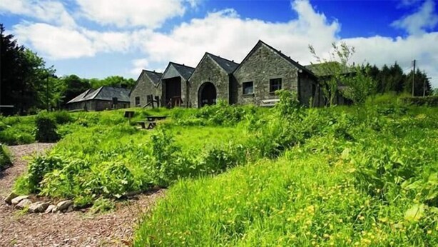 A row of stone buildings with arched doorways, surrounded by lush greenery.