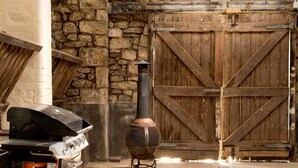 A rustic outdoor area with a stone wall, a wooden door, and a wood-burning stove.