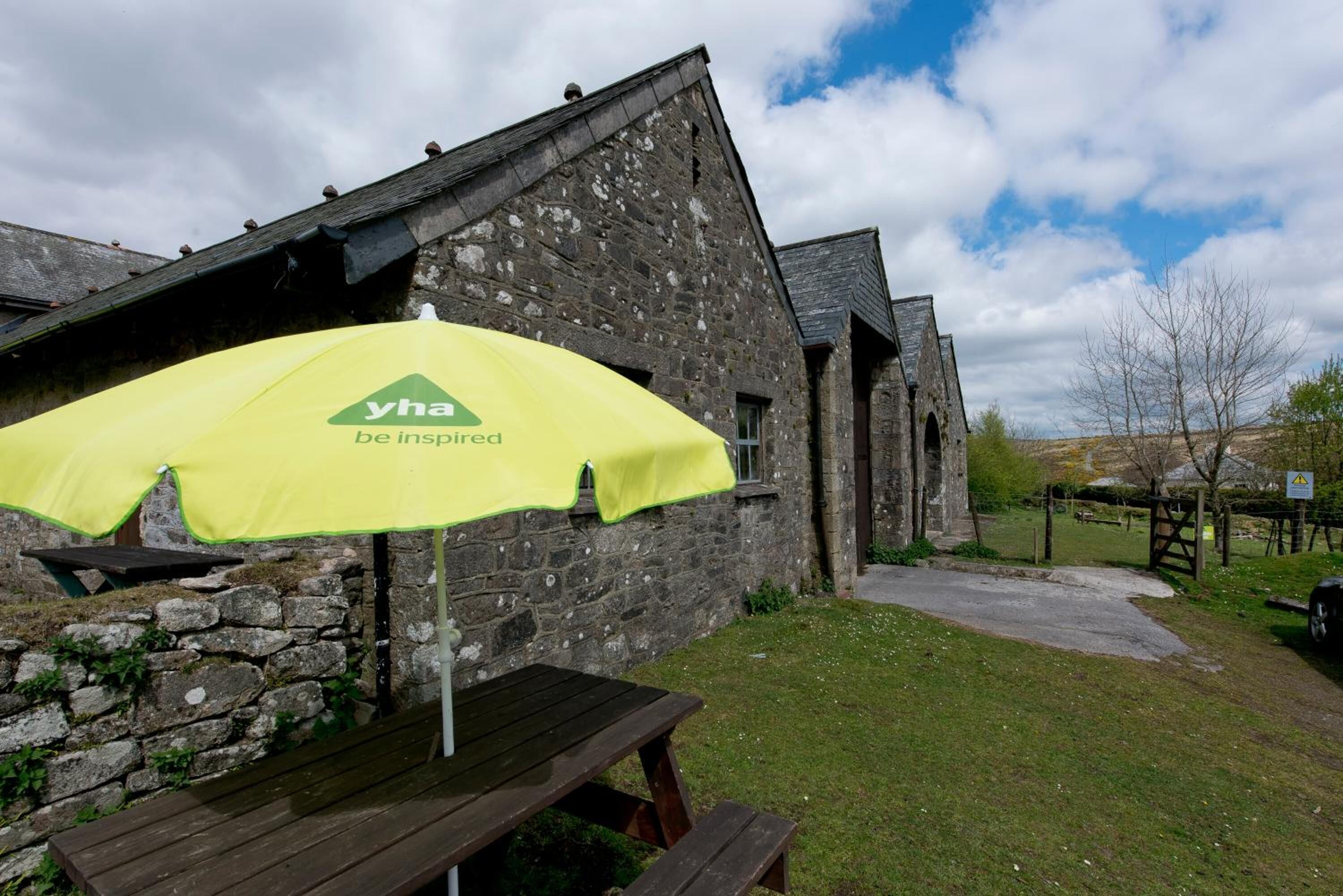 A stone building with a yellow umbrella labeled "yha be inspired" and a picnic table in front.