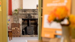 A cozy room with a stone fireplace, a wicker basket of firewood, and a small table with a vase of flowers.